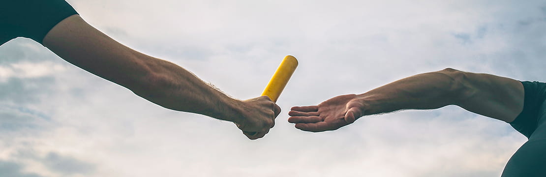 Two people pass a relay baton during a race, symbolizing how board leadership creates lasting impact by sharing responsibility, guiding mission-driven work and strengthening communities for future generations.